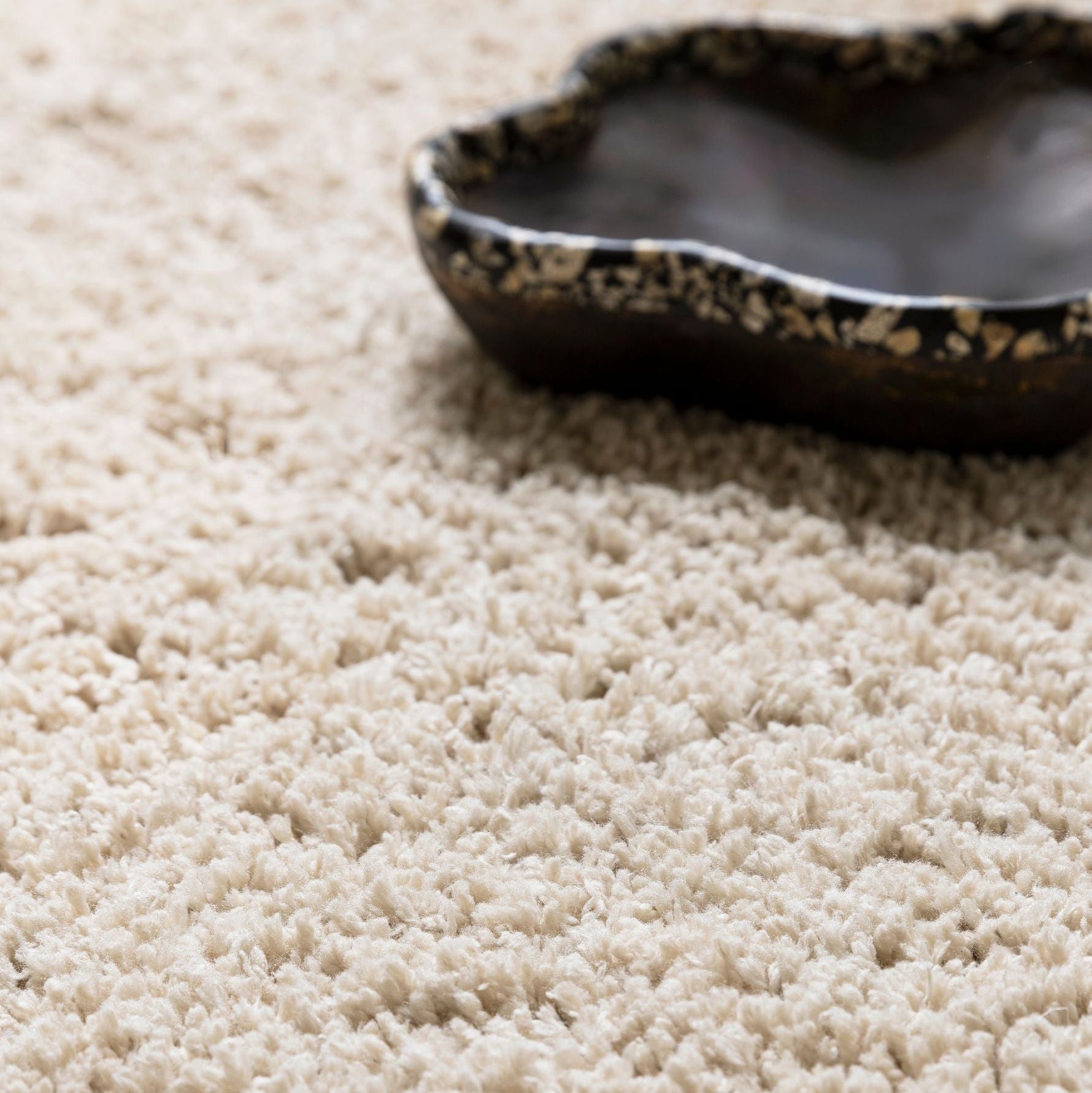 Celeste vloerkleed van MUST Living in beige, close-up van de lange pool met donkere schaal erop