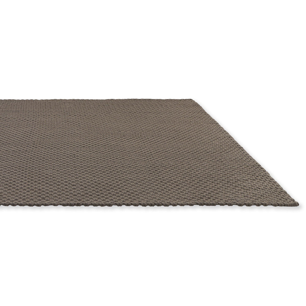 Het Nomad outdoor tapijt in Grey Taupe onder een loungeset op het terras