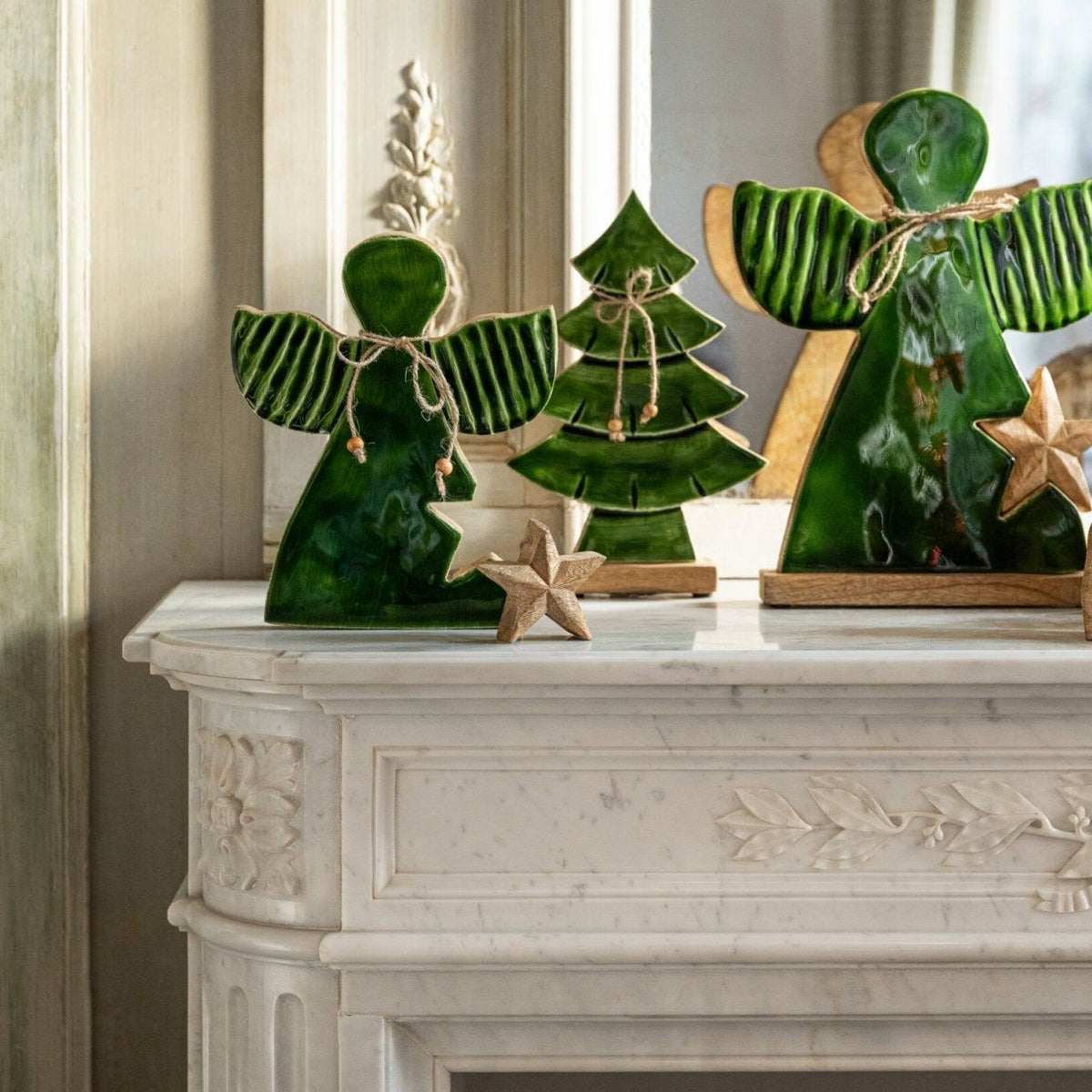 Kerstengelen Met Ster van J-Line op een witte schouw, met houten kerstboompje en kerststal ernaast