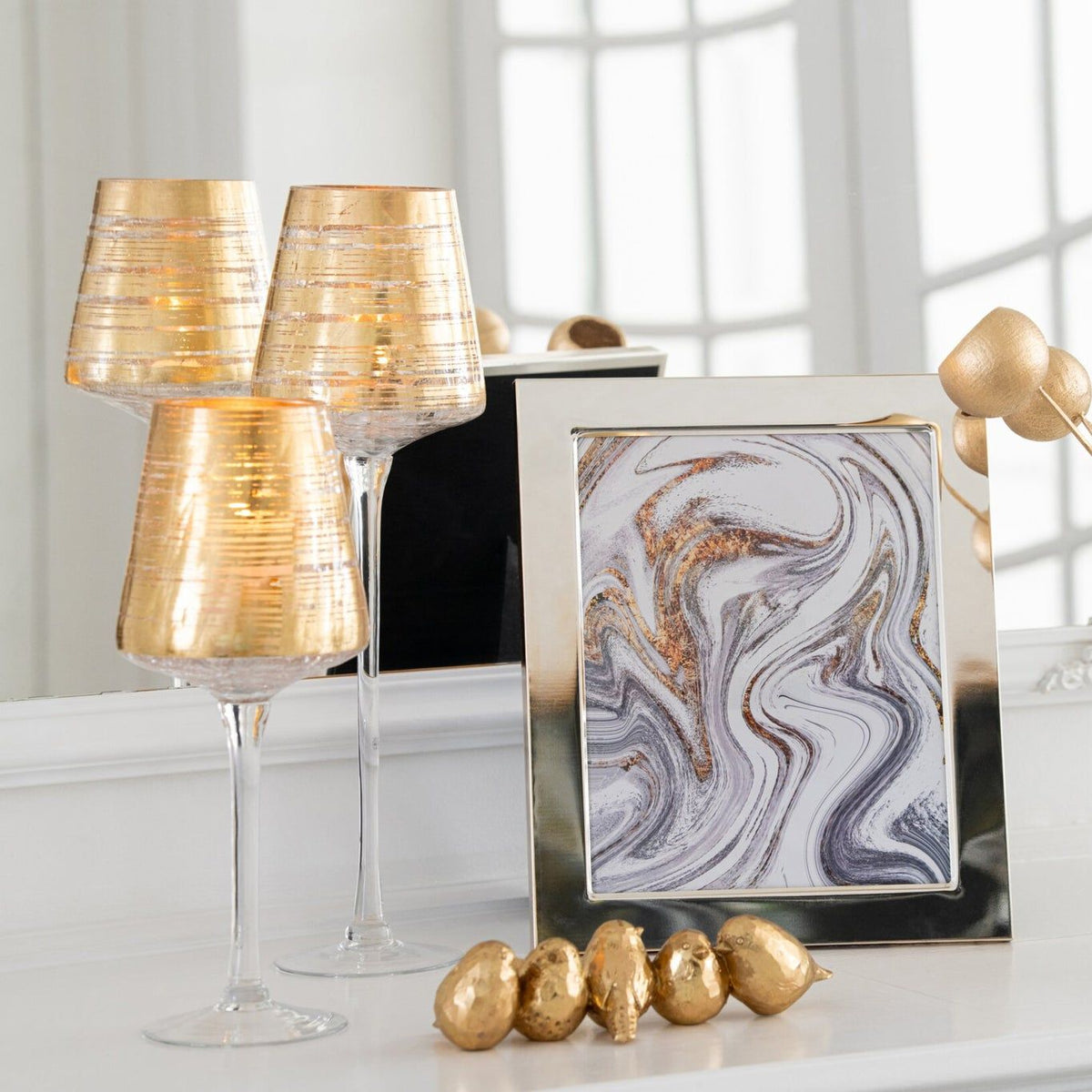 Gouden windlichten op voet van J-Line op een schouw naast een lijst en decoratie