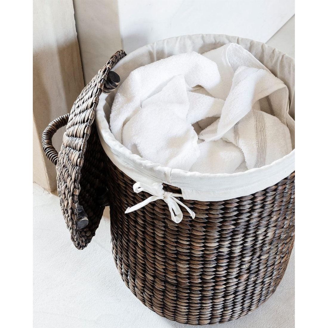 Wasmand Tahiti van MUST Living naast een bed, gevuld met linnengoed