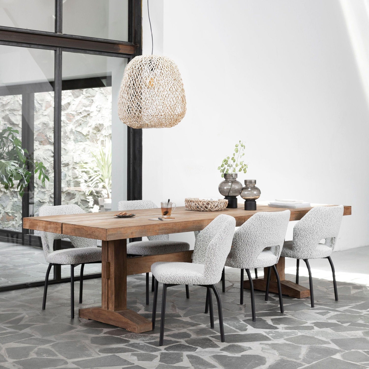 Eetkamerstoel Bloom van MUST Living in licht grijs bouclé aan een houten eettafel in een lichte eetkamer