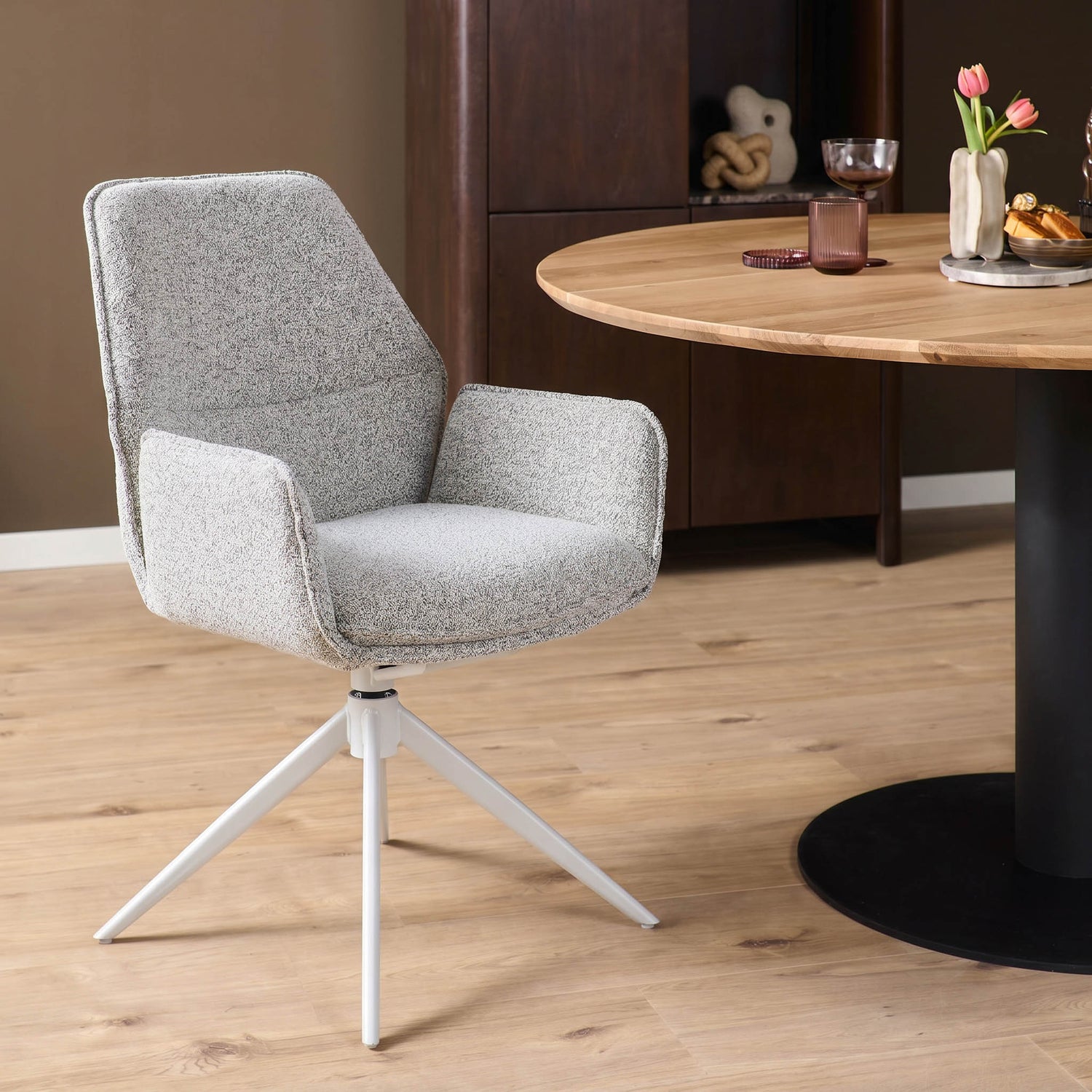 Lichtgrijze eetkamerstoel Hera met armleuningen aan een ronde houten eettafel