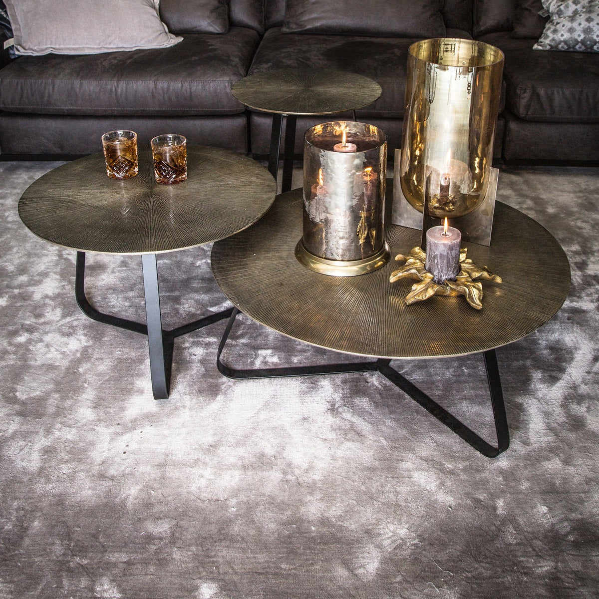 Kae salontafel Medium van PTMD naast een kleinere Kae tafel, goud aluminium bladen met zwart onderstel op vloerkleed