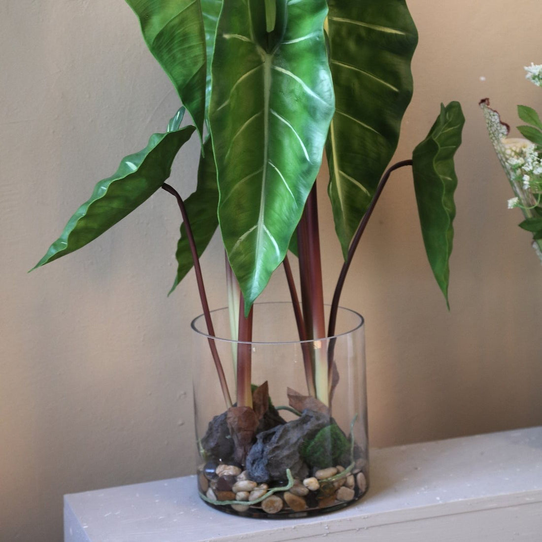 Kunstphilodendron van PTMD in glazen vaas gestyled op een dressoir