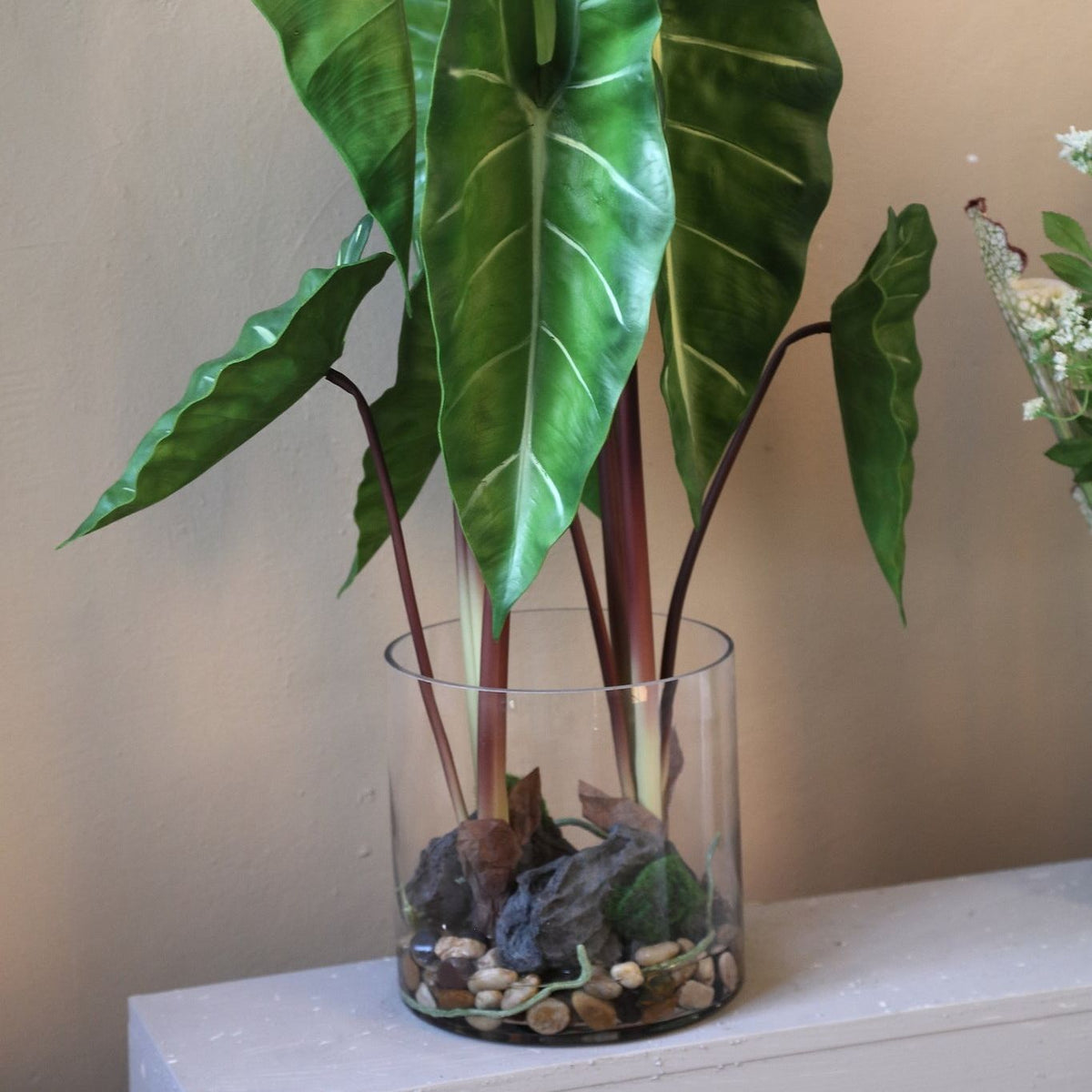 Kunstphilodendron van PTMD in glazen vaas gestyled op een dressoir