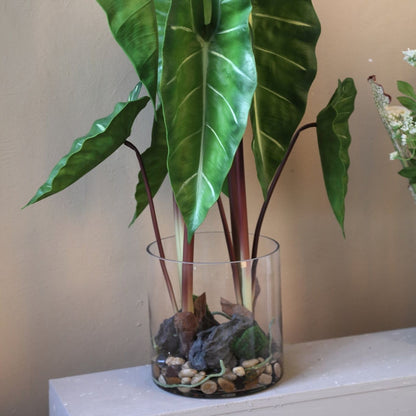 Kunstphilodendron van PTMD in glazen vaas gestyled op een dressoir
