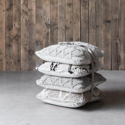 Ivoorkleurig wollen kussen Dolomite van MUST Living op een fauteuil in een warme woonkamer