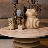 Malines Kandelaar Goud van PTMD met kaars op een ronde salontafel naast een geribbelde vaas