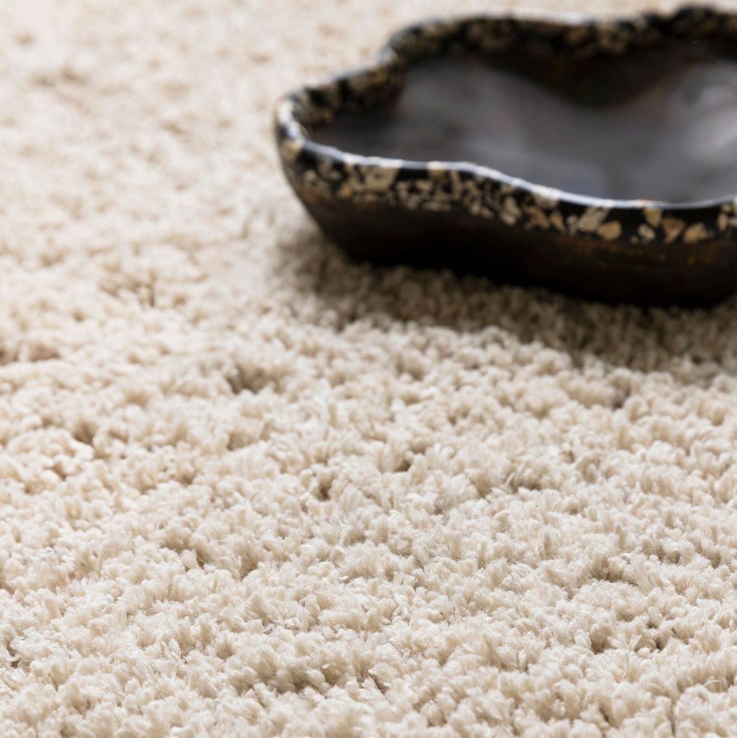 Celeste vloerkleed van MUST Living in beige, close-up van de lange pool met donkere schaal erop