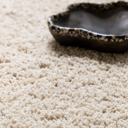 Celeste vloerkleed van MUST Living in beige, close-up van de lange pool met donkere schaal erop