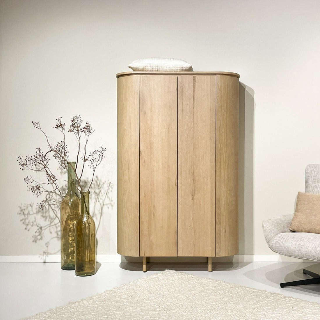 Naturel eiken Tobago opbergkast in een kamer met fauteuil en vaas met droogbloemen