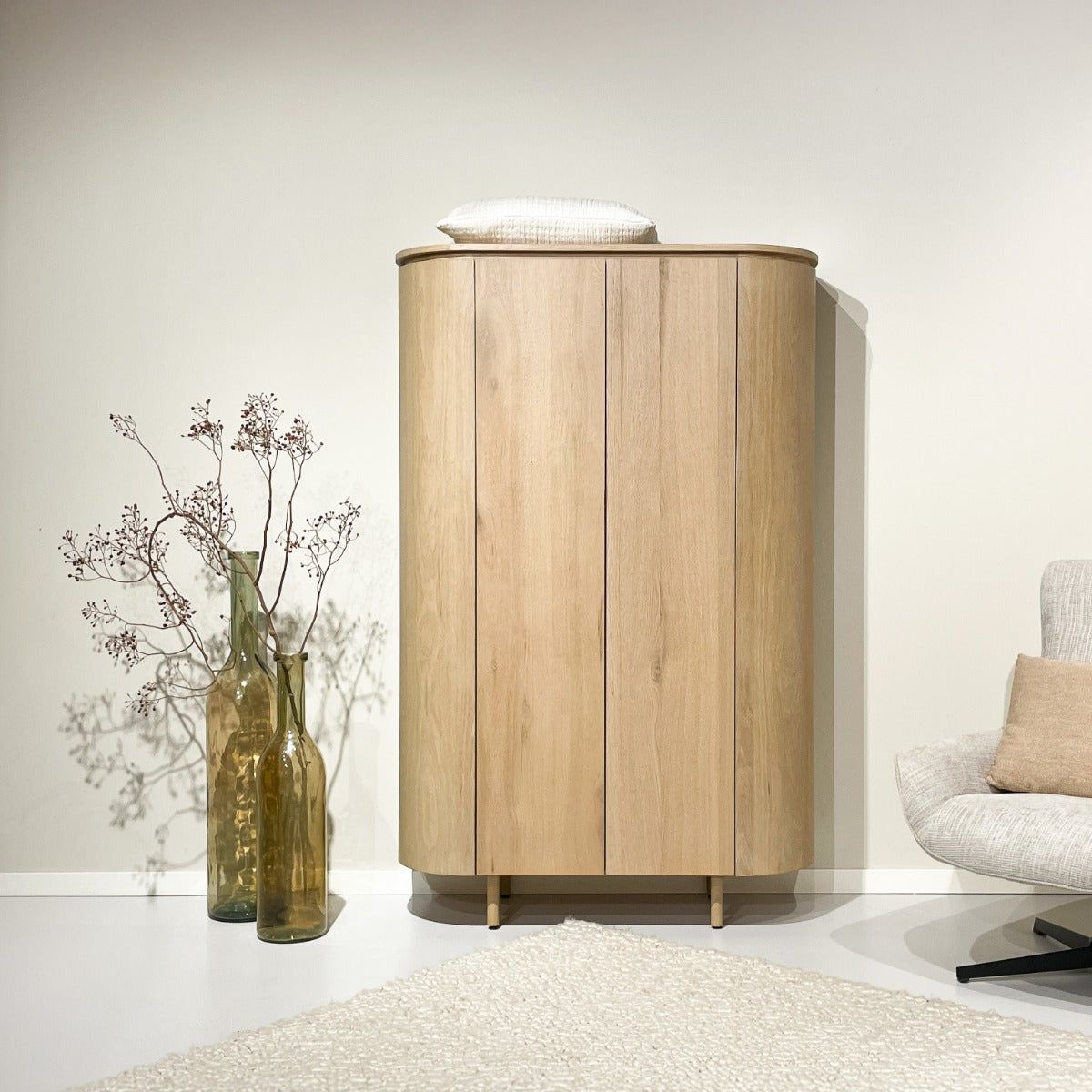 Naturel eiken Tobago opbergkast in een kamer met fauteuil en vaas met droogbloemen