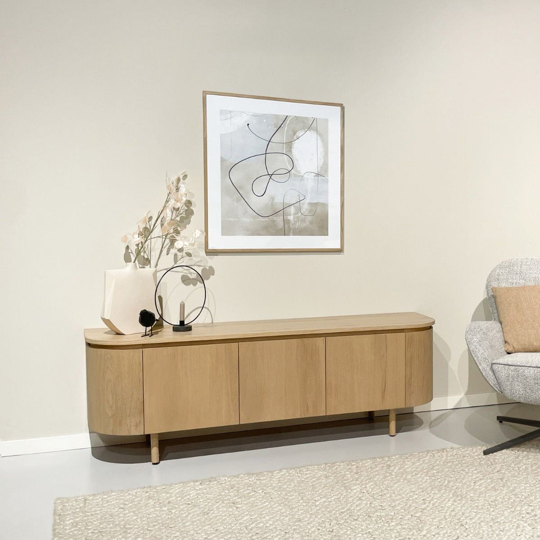 TV-meubel Tobago in naturel eiken in een woonkamer met fauteuil en lijst aan de wand